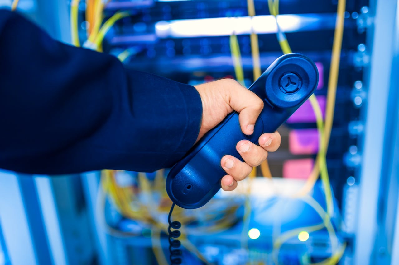 services-02 Close-up of a hand holding a telephone receiver in a server room emphasizing technology.